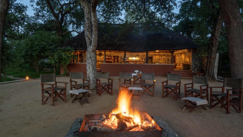 Campfire and surrounding chairs with Thawale Lodge accommodation in the background